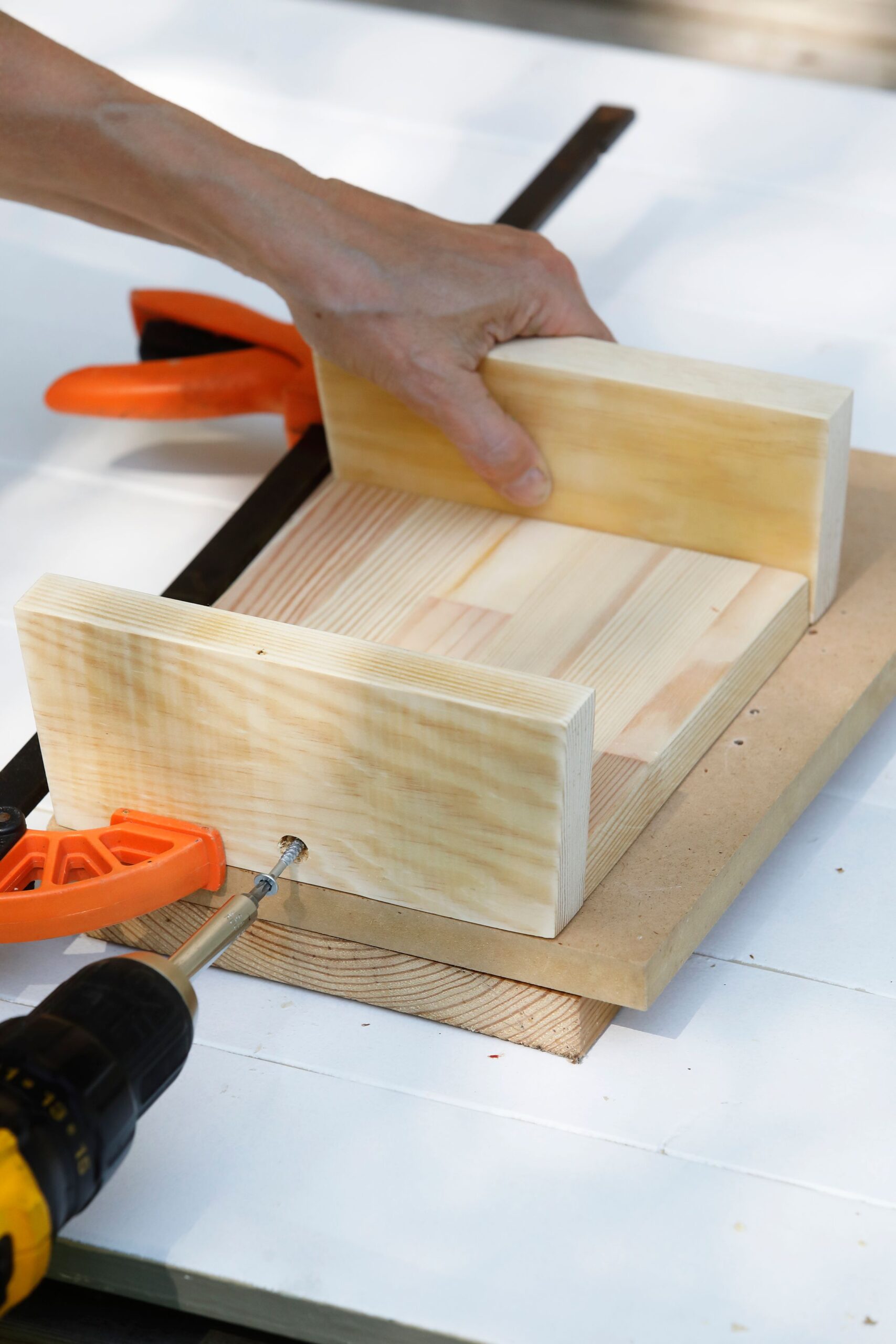 Laita taso työpöydälle parin ylimääräisen aluslevyn päälle. Kiinnitä siihen viistojen lautojen kapeampi reuna yhdellä ruuvilla: poraa keskelle tappiporalla upotus ja kiinnitä ruuvi. Kiinnitä samoin vastakkainen lauta.